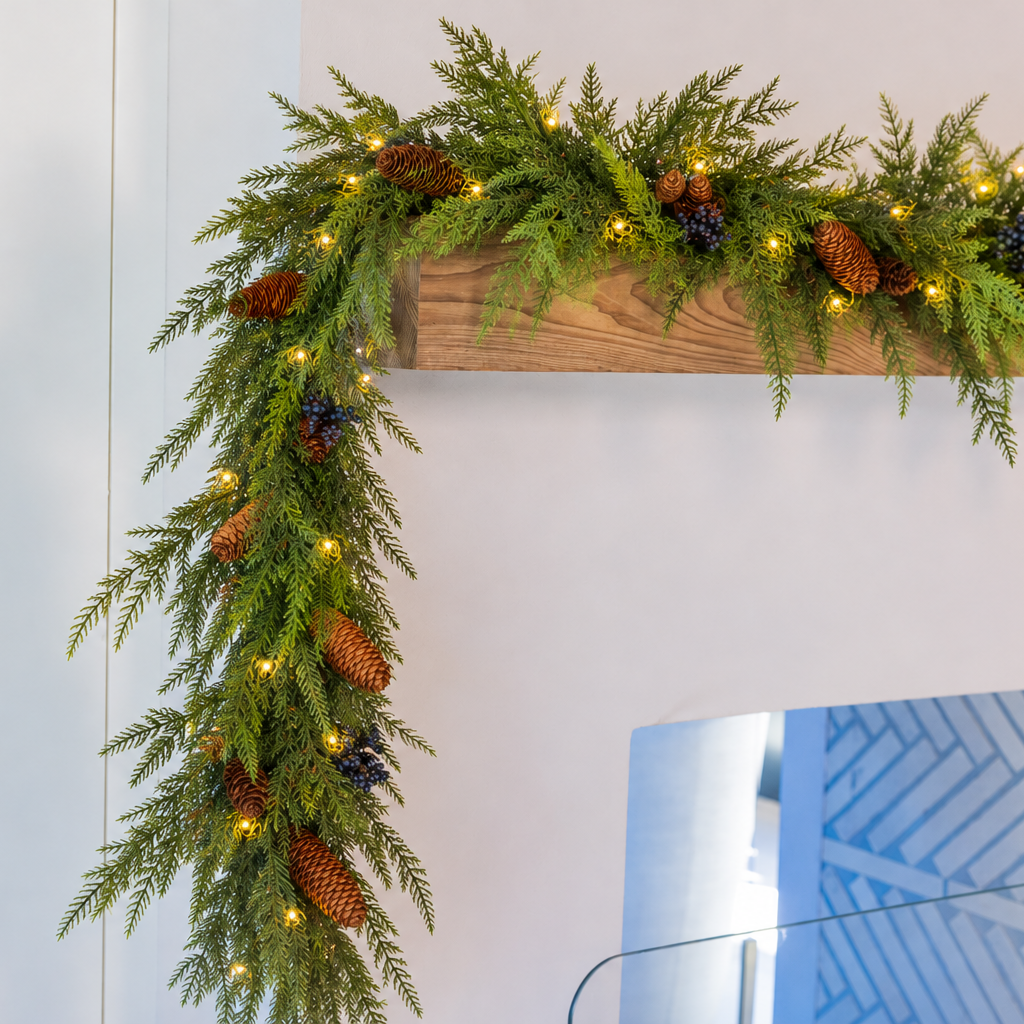Deep green soft touch norfolk pine and cedar tips garland adorned with lifelike blueberries, real pinecone clusters, and warm white fairy LED lights