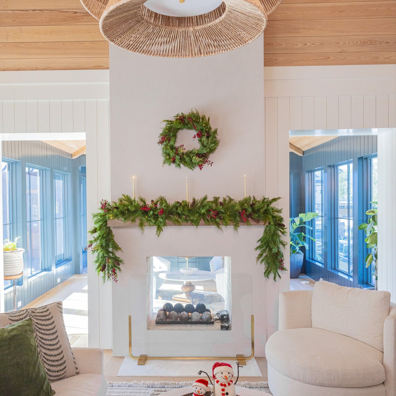 Pre-lit Plymouth Christmas wreath hung over the mantel in a light living room with berry garland and taper candles