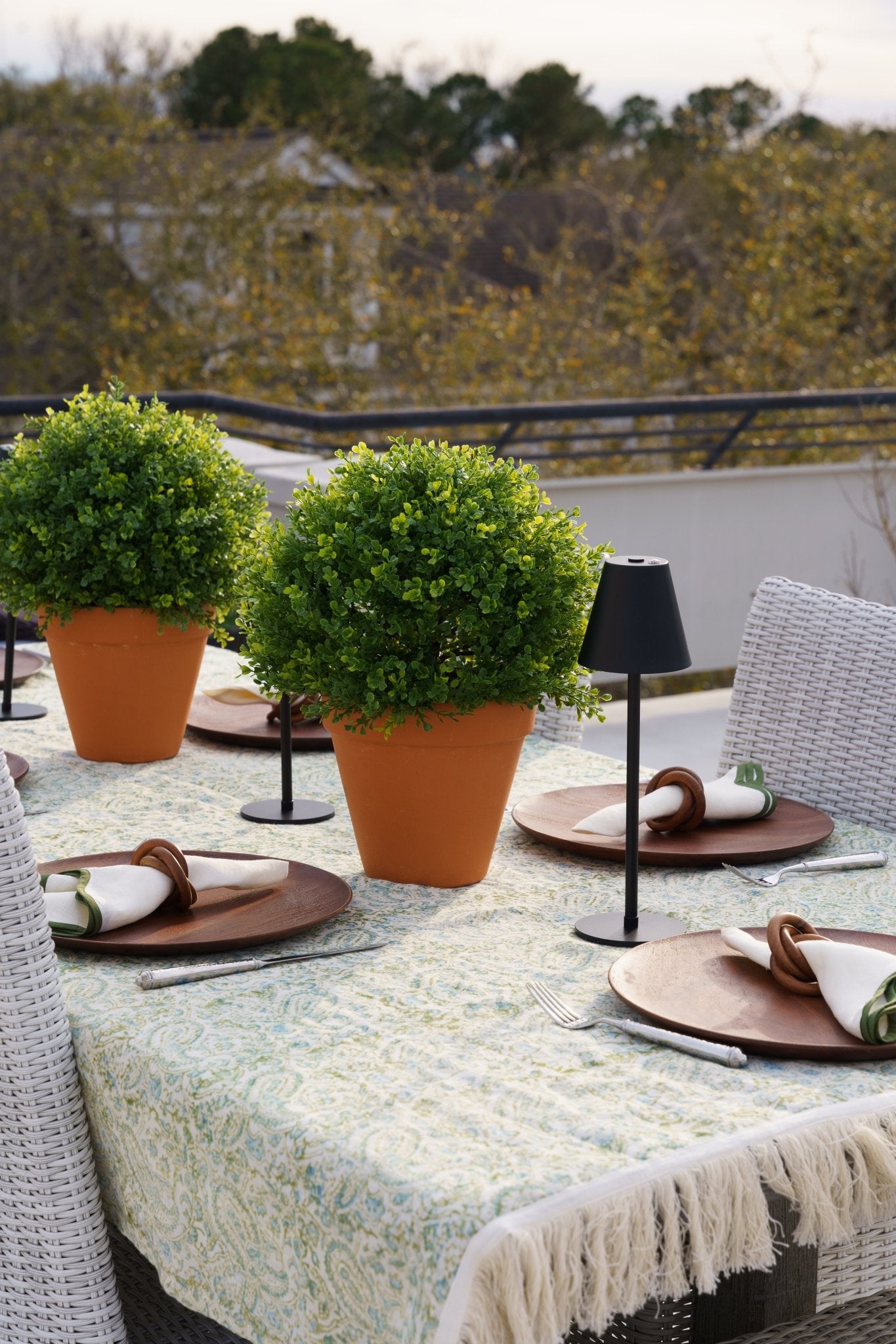 Artificial boxwood spheres in terracotta pots used as centerpieces on an outdoor dining table