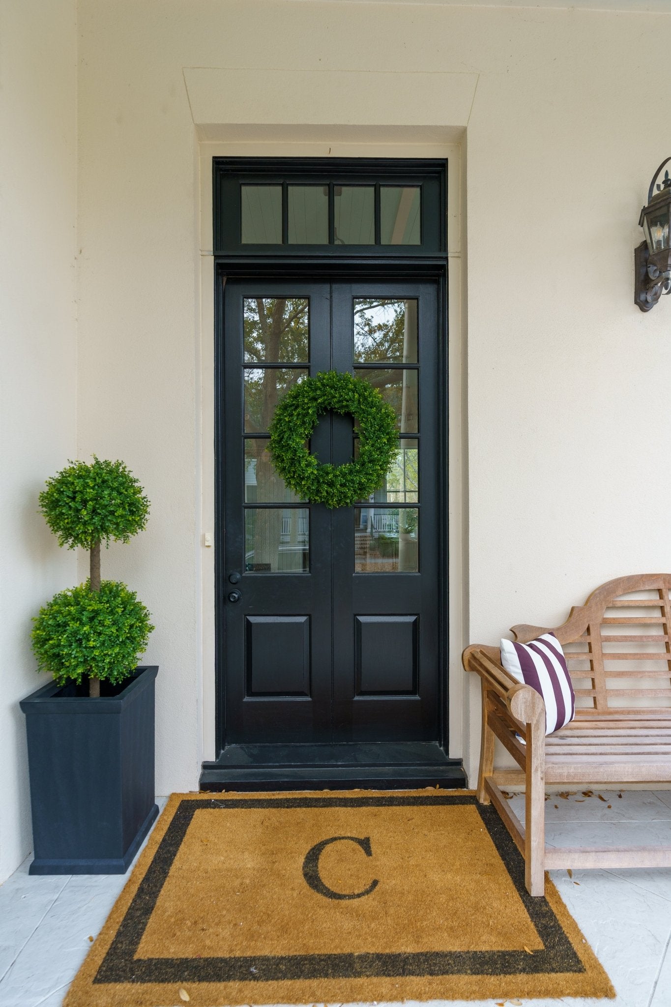 Artificial boxwood double topiary sphere in a charcoal planter beside a black door with a boxwood wreath